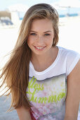 A young blonde woman on a beach wearing a colourful t-shirt