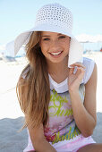 A young blonde woman on a beach wearing a colourful t-shirt and a white summer hat