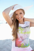 A young blonde woman on a beach wearing a colourful t-shirt and a white summer hat