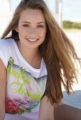 A young blonde woman on a beach wearing a colourful t-shirt