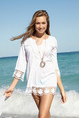 Junge blonde Frau mit weißem Sommerhut in weißem Sommerkleid am Strand