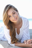 A young blonde woman on a beach wearing a white summer dress