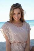 A young blonde woman on a beach wearing a beige polka-dot dress