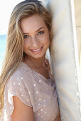 A young blonde woman on a beach wearing a beige polka-dot dress