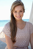 A young blonde woman on a beach wearing a beige polka-dot dress