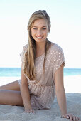 A young blonde woman on a beach wearing a beige polka-dot dress