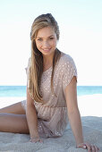 A young blonde woman on a beach wearing a beige polka-dot dress