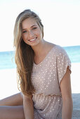 A young blonde woman on a beach wearing a beige polka-dot dress