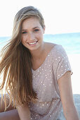 A young blonde woman on a beach wearing a beige polka-dot dress