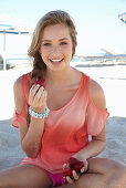 A young blonde woman on a beach wearing a salmon-coloured, off-the-shoulder top