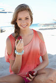 A young blonde woman on a beach wearing a salmon-coloured, off-the-shoulder top