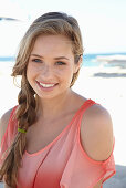 A young blonde woman on a beach wearing a salmon-coloured, off-the-shoulder top