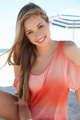 Junge blonde Frau in lachsfarbenem schulterfreiem Top am Strand