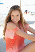 A young blonde woman on a beach wearing a salmon-coloured, off-the-shoulder top