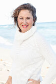 A brunette woman on a beach wearing a white knitted jumper