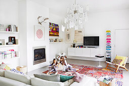 Weißes Wohnzimmer mit bunten Accessoires, lesende Mädchen auf dem Teppich