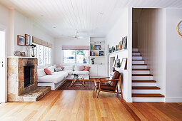 Sandstone fireplace in lounge with white wooden ceiling, next to staircase