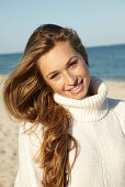 A young blonde woman on a beach wearing a white turtle neck jumper