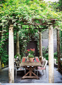 Rustic wooden table with chairs under pergola with wisteria