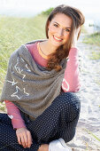 A brunette woman wearing a grey shawl and a pink knitted jumper with heats