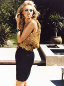 A young blonde woman posing in the garden of a house wearing a black evening dress