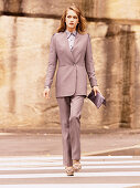 A young woman wearing a purple trouser suit with a blouse and a bag