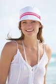 A young brunette woman on a beach wearing a white top and a white hat