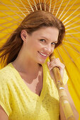 A young brunette woman wearing a yellow shirt holding a parasol