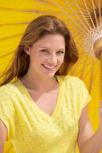 A young brunette woman wearing a yellow shirt holding a parasol