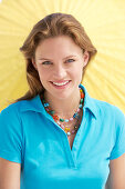 A young brunette woman wearing a blue shirt in front of a yellow parasol