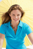 A young brunette woman wearing a blue shirt in front of a yellow parasol