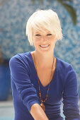 A mature blonde woman with short hair wearing a blue top against a blue background