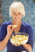 A mature blonde woman with short hair wearing a blue top with a bowl of pineapple