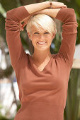 A mature blonde woman with short hair outside wearing a brown top