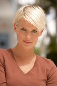 A mature blonde woman with short hair outside wearing a brown top