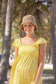 A mature blonde woman with short hair outside wearing a yellow top and a hat