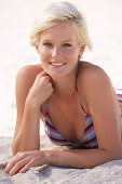 A mature blonde woman with short hair on a beach wearing a striped bikini