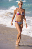 Reife, kurzhaarige blonde Frau im gestreiften Bikini am Strand