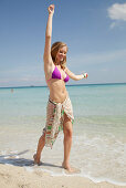 Junge blonde Frau im lila Bikini und Strandtuch um die Hüften am Strand