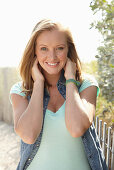 A young blonde woman outside wearing a sleeveless denim jacket and a light-blue top