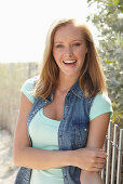 A young blonde woman outside wearing a sleeveless denim jacket and a light-blue top