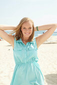 A young blonde woman on a beach wearing a light-blue summer dress