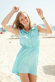A young blonde woman on a beach wearing a light-blue summer dress