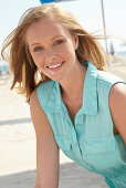 A young blonde woman on a beach wearing a light-blue summer dress