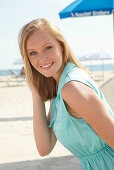 A young blonde woman on a beach wearing a light-blue summer dress