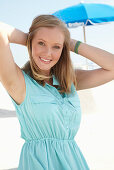 A young blonde woman on a beach wearing a light-blue summer dress