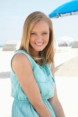 A young blonde woman on a beach wearing a light-blue summer dress