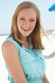 A young blonde woman on a beach wearing a light-blue summer dress