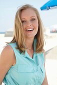 A young blonde woman on a beach wearing a light-blue summer dress