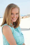 A young blonde woman on a beach wearing a light-blue summer dress